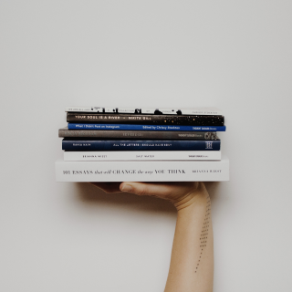 Photo of an arm up with the hand at 90 degrees holding seven stacked books.